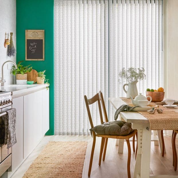 White patterned vertical blinds covering a sliding glass door, closed and softly diffusing daylight; cozy kitchen-dining space with teal accent wall, wooden table and chairs, plants, jute rug.

Text: have a good day
