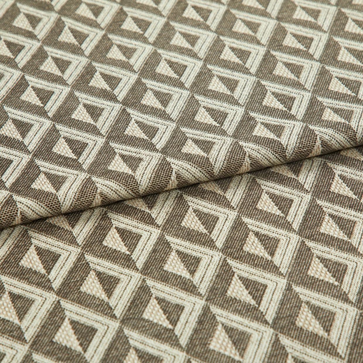 Woven upholstery fabric with repeating cream and brown triangular geometric pattern; folded across the middle, lying flat; close-up studio lighting emphasizes texture and tight weave.