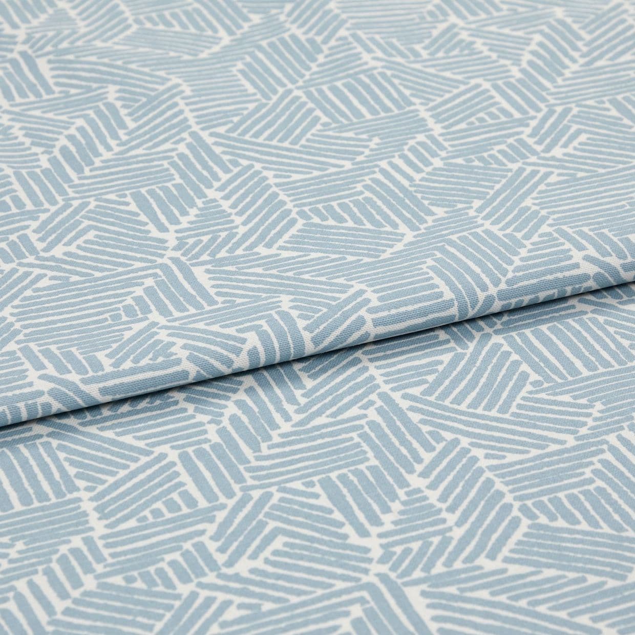 Light blue-and-white patterned fabric with geometric short parallel-stripe blocks; folded with an overlapping edge; close-up on textile surface under soft, even studio lighting.