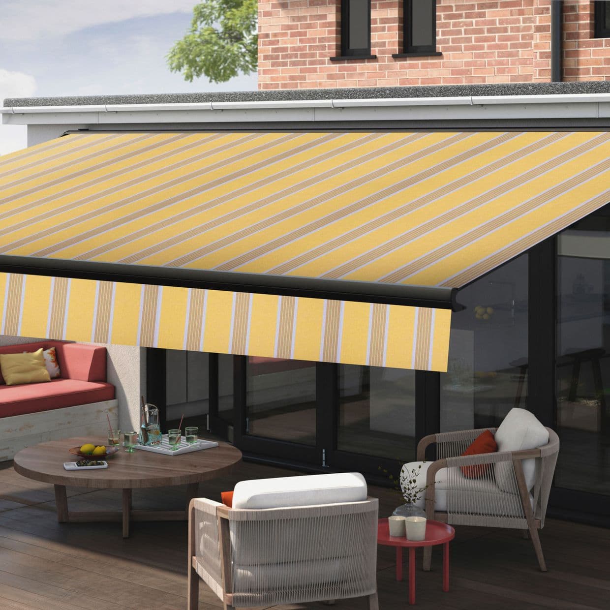 Yellow-striped retractable awning extended over a patio, shading outdoor seating and a wooden table; modern brick house with large glass doors, wood decking, potted plant and tree in daylight.