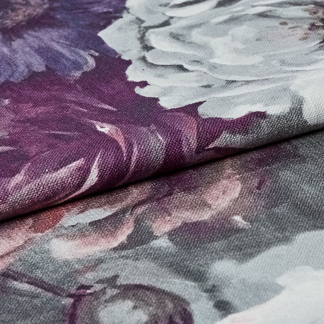 Folded floral-printed canvas fabric (textured weave), edge overlapping and creating a ridge; showing white and purple peony-like petals in a close-up macro view with soft, even lighting.