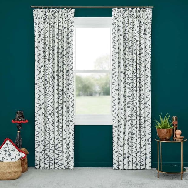 White curtains with black zigzag print, pleated and hung on a rod, pulled aside to frame a closed window; soft daylight views of a blurred lawn in a teal-walled room.