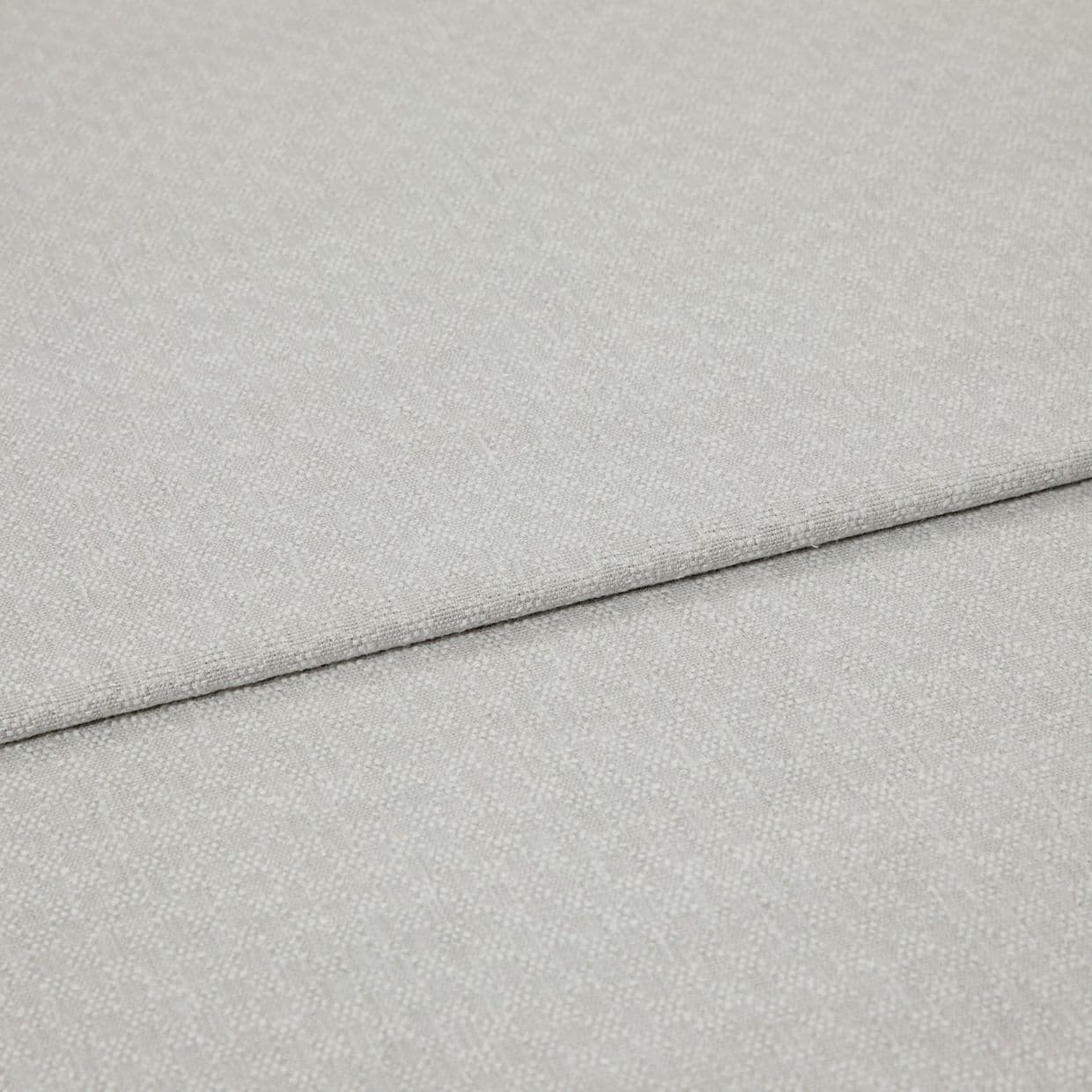 Light grey textured fabric panels overlapping slightly; top panel folded along a seam. Close-up view emphasizing woven pebble pattern, soft matte lighting, minimal background, studio-like neutral setting.