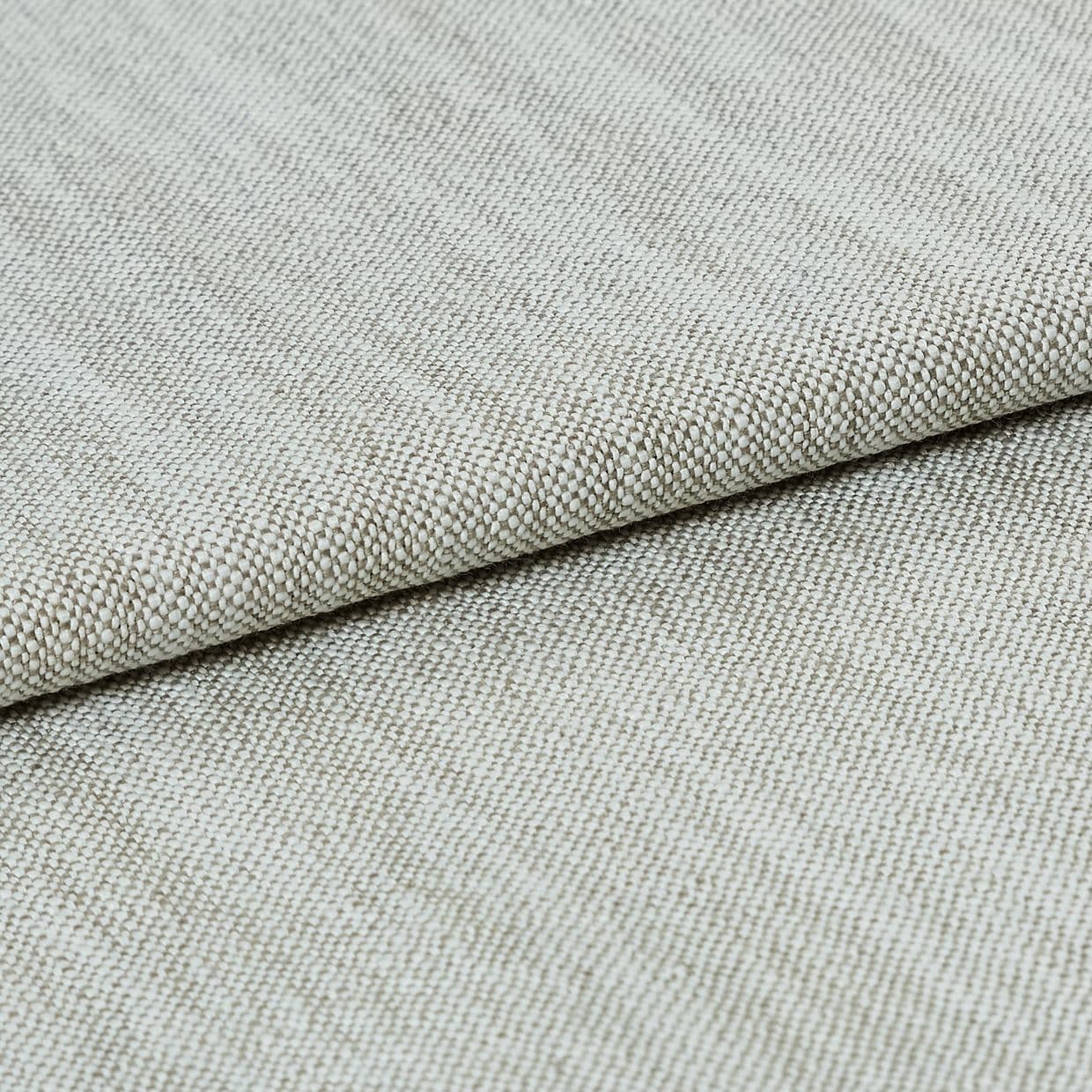 A beige, tightly woven upholstery fabric folded once, revealing a textured basket-weave edge; lying flat on a neutral surface under soft, even studio lighting.