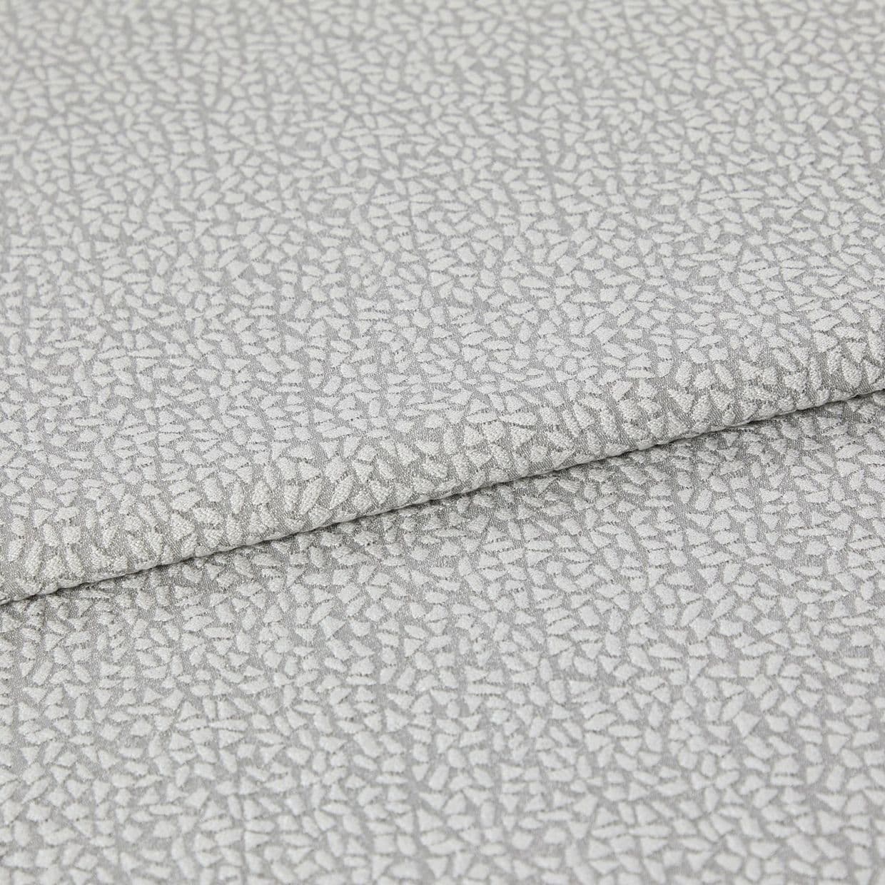 Light-gray, pebble-patterned upholstery fabric folded once, textured with a subtle metallic sheen; close-up view on a neutral surface under soft, diffuse lighting.