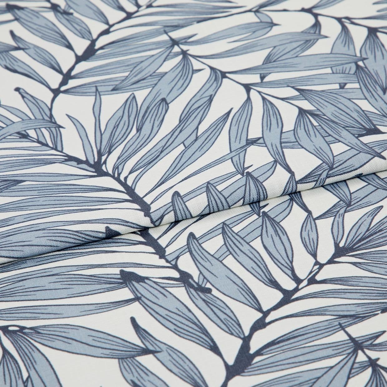 Blue botanical-print fabric (fine woven textile with navy stems and pale blue elongated leaves) folded and layered, edges overlapping; close-up view on a white surface with soft, diffused lighting.