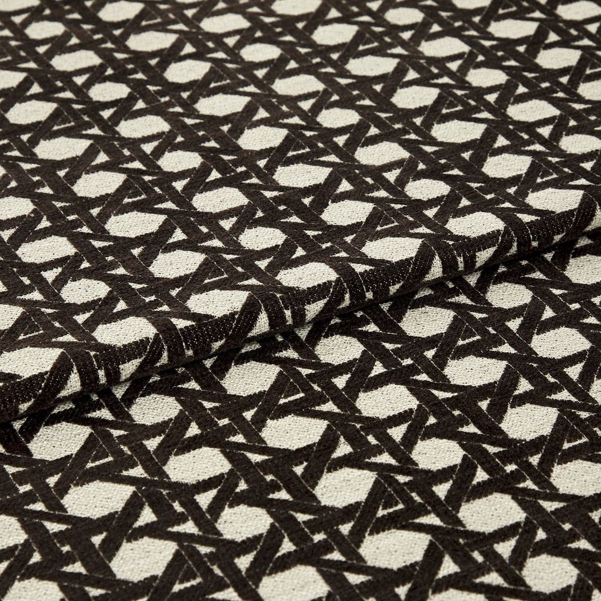 Woven beige fabric with dense black geometric lattice pattern, folded over itself; repeating circular-and-cross motif, textured upholstery cloth displayed flat under neutral studio lighting.