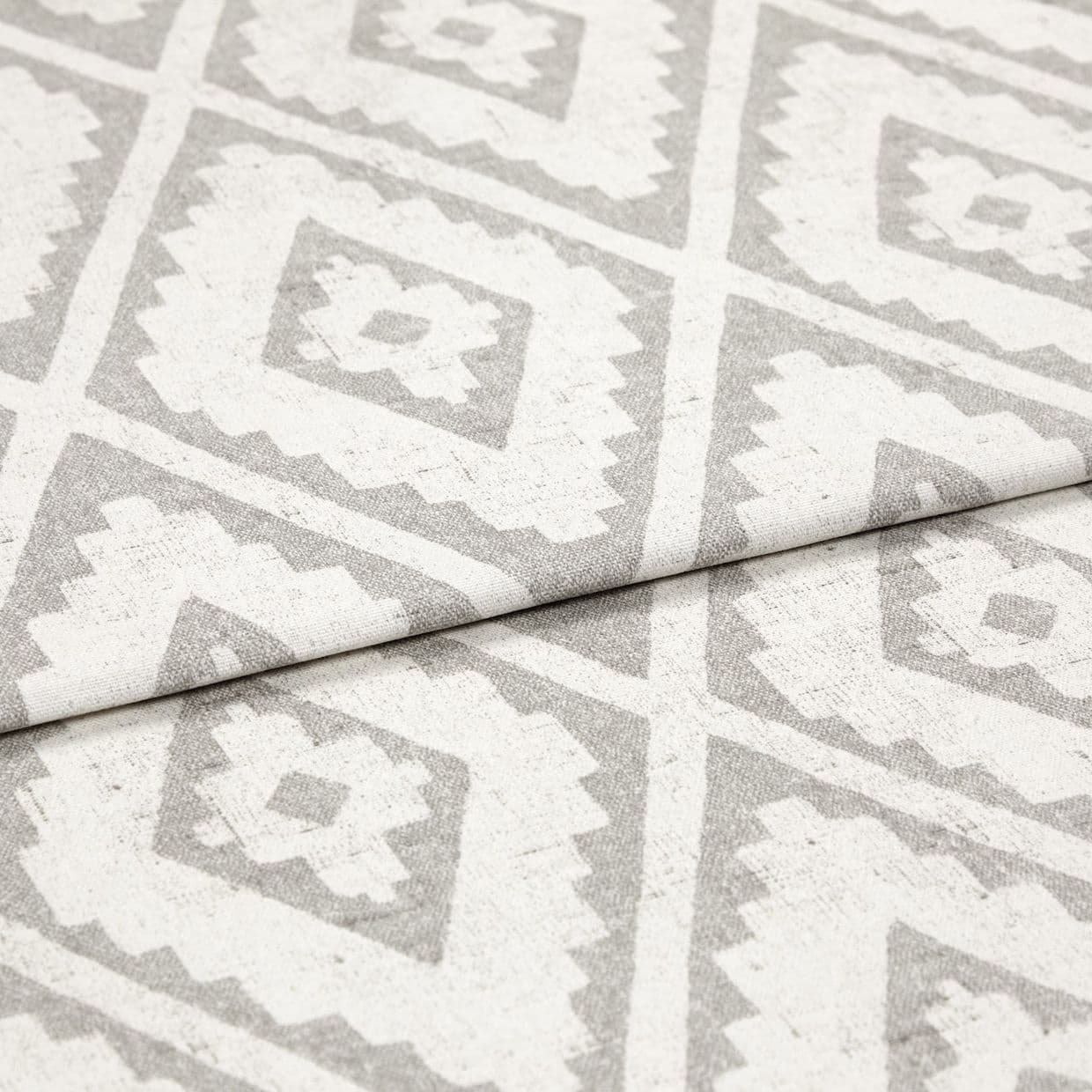 Woven rug with repeating gray diamond-and-zigzag pattern, shown folded once across the center; textured fabric lies flat in soft, even studio lighting, close-up detail view.