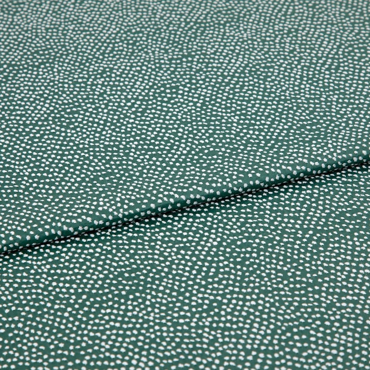 Speckled green fabric (small irregular white dots) folded across center, creating a shallow overlapping crease; close-up on a flat, evenly lit textile sample.