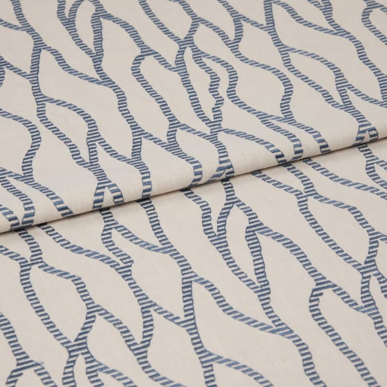 Beige fabric with repeating blue rope-like chain pattern, folded and layered across itself; close-up on a flat surface with soft, even lighting that emphasizes the woven texture.
