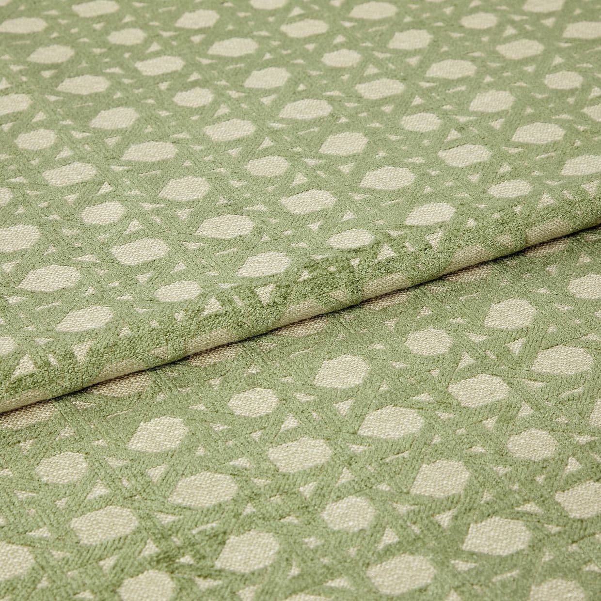 Green patterned woven fabric with raised geometric dots and lattice, folded over itself and showing textured pile; close-up studio view with soft, even lighting emphasizing the fibers.