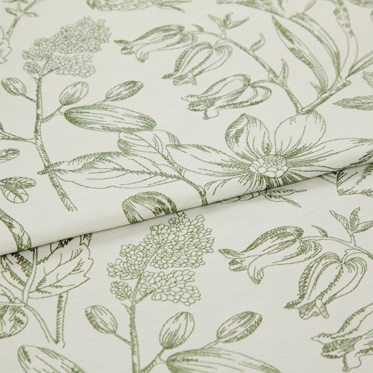 Folded curtain fabric with green line-drawn botanical print; overlapping fold reveals large floral and bud motifs, laid flat in a close-up studio view with soft, neutral lighting.