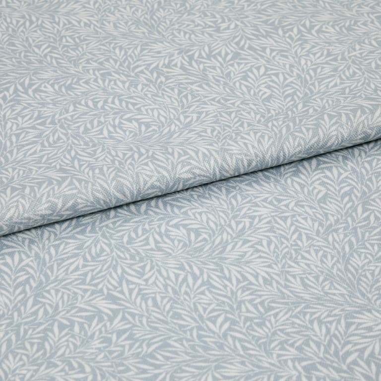 Light-blue printed fabric with a white leaf motif folded once and overlapping; close-up of a soft woven textile surface under even, neutral lighting.