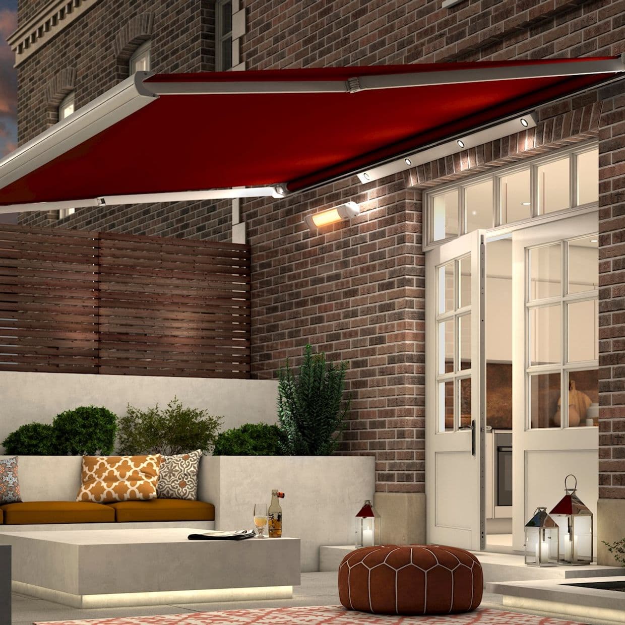 A red retractable awning extends from a brick exterior above open French doors, shading a modern patio with built-in bench seating, potted greenery, warm evening lighting, and decorative lanterns.