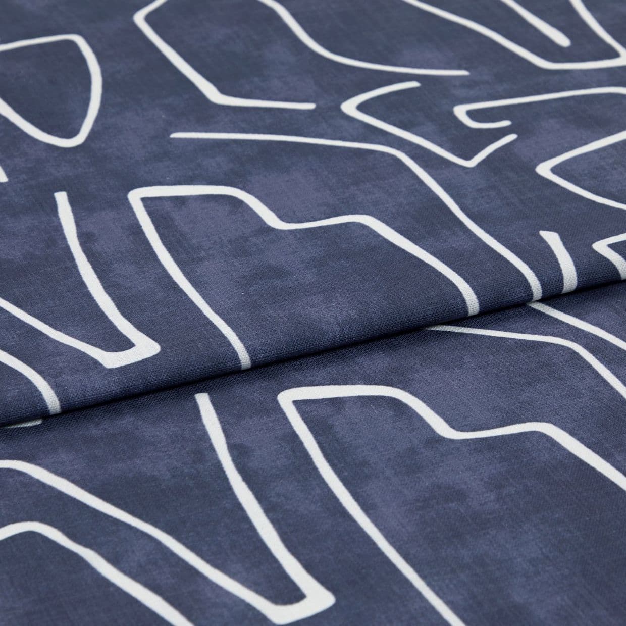 Navy-blue fabric with white abstract linear print, folded once; fabric rests flat, studio-lit close-up revealing woven texture and a visible fold/seam.