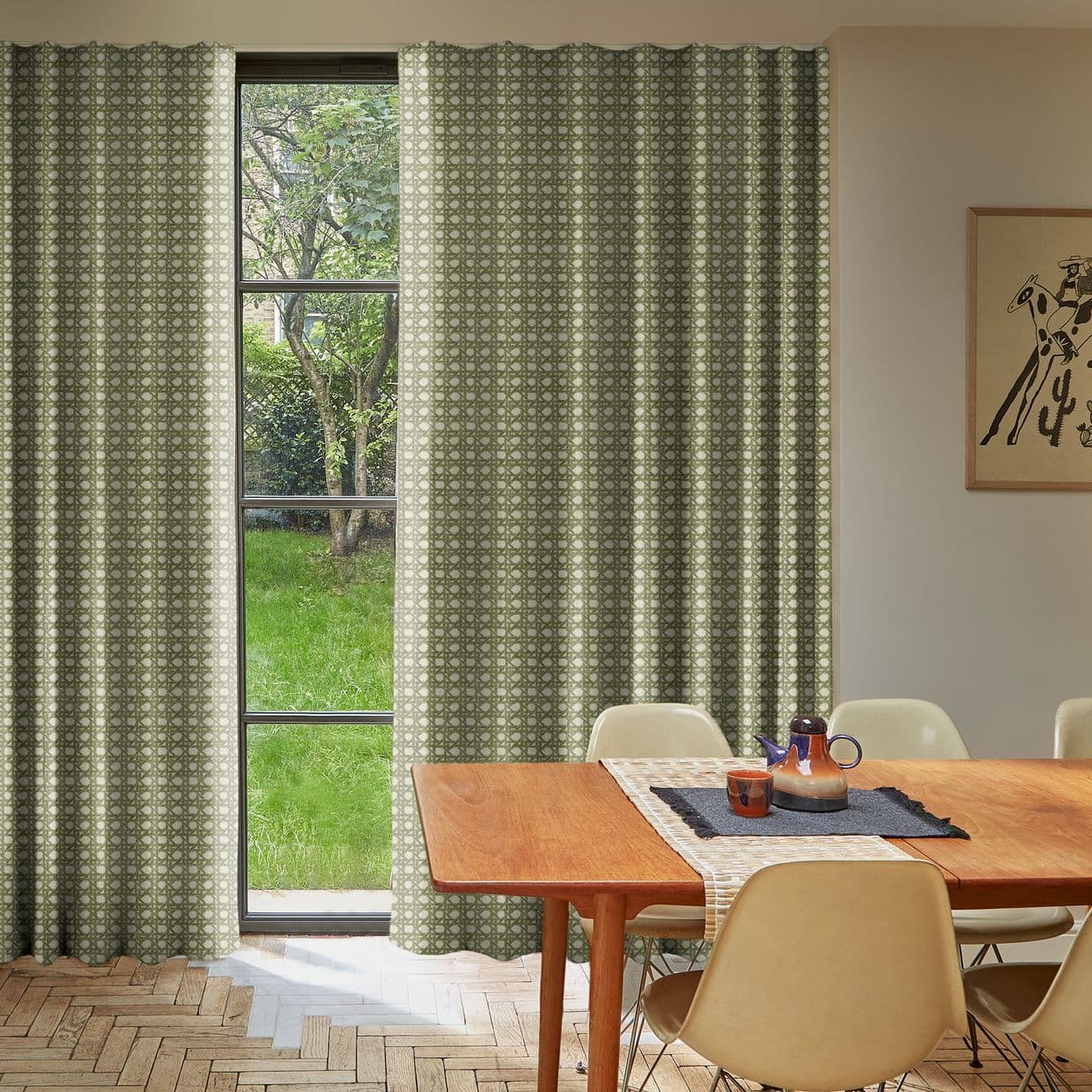 Patterned green curtains, full-length pleated panels drawn mostly closed, filtering daylight through a tall multi-pane window; dining table and chairs in sunlit room, grassy backyard and tree visible outside.