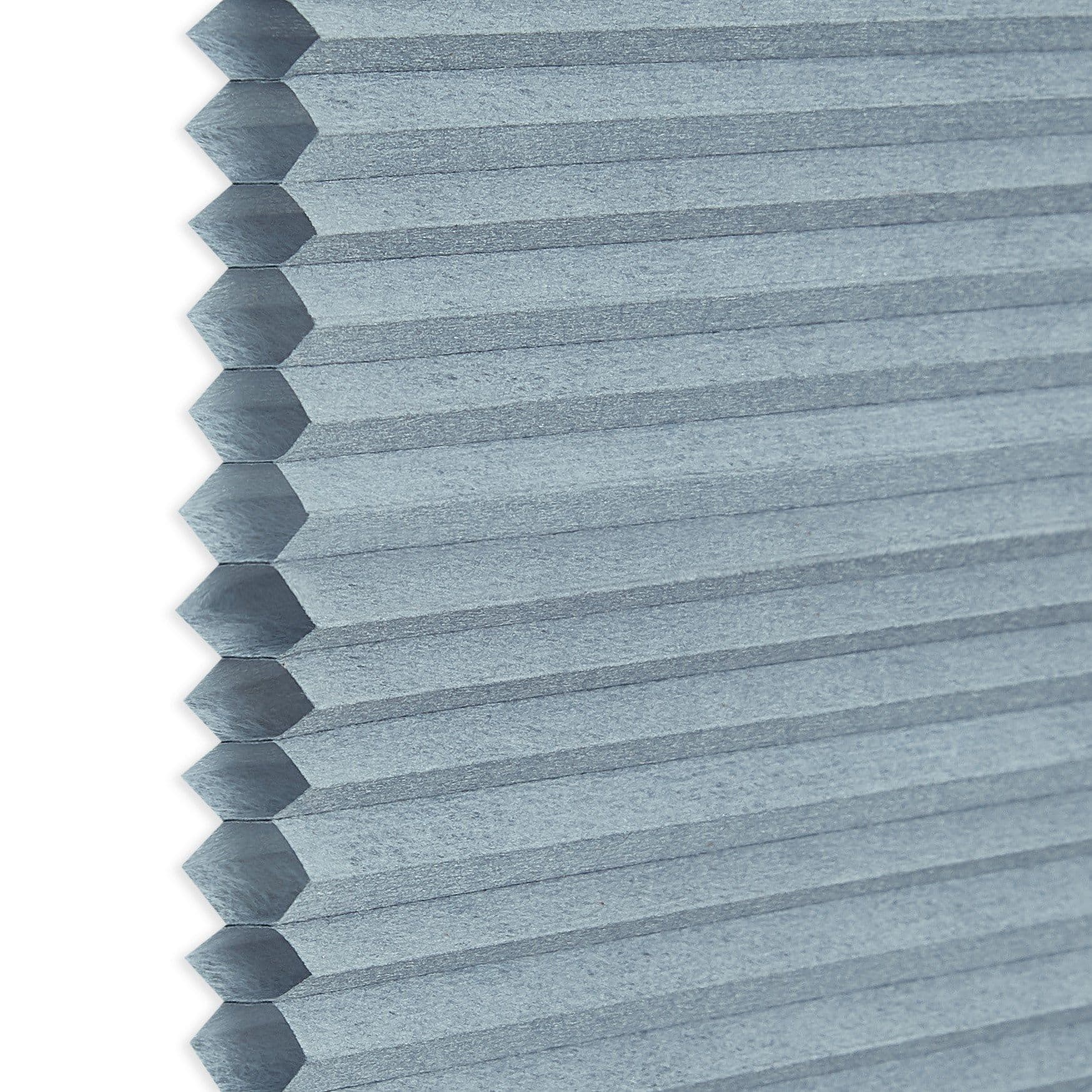 A light-blue honeycomb (cellular) blind, hexagonal cells visible along the left edge; closed into uniform horizontal pleats, blocking view and filtering light, shown in a close-up with soft, neutral lighting.