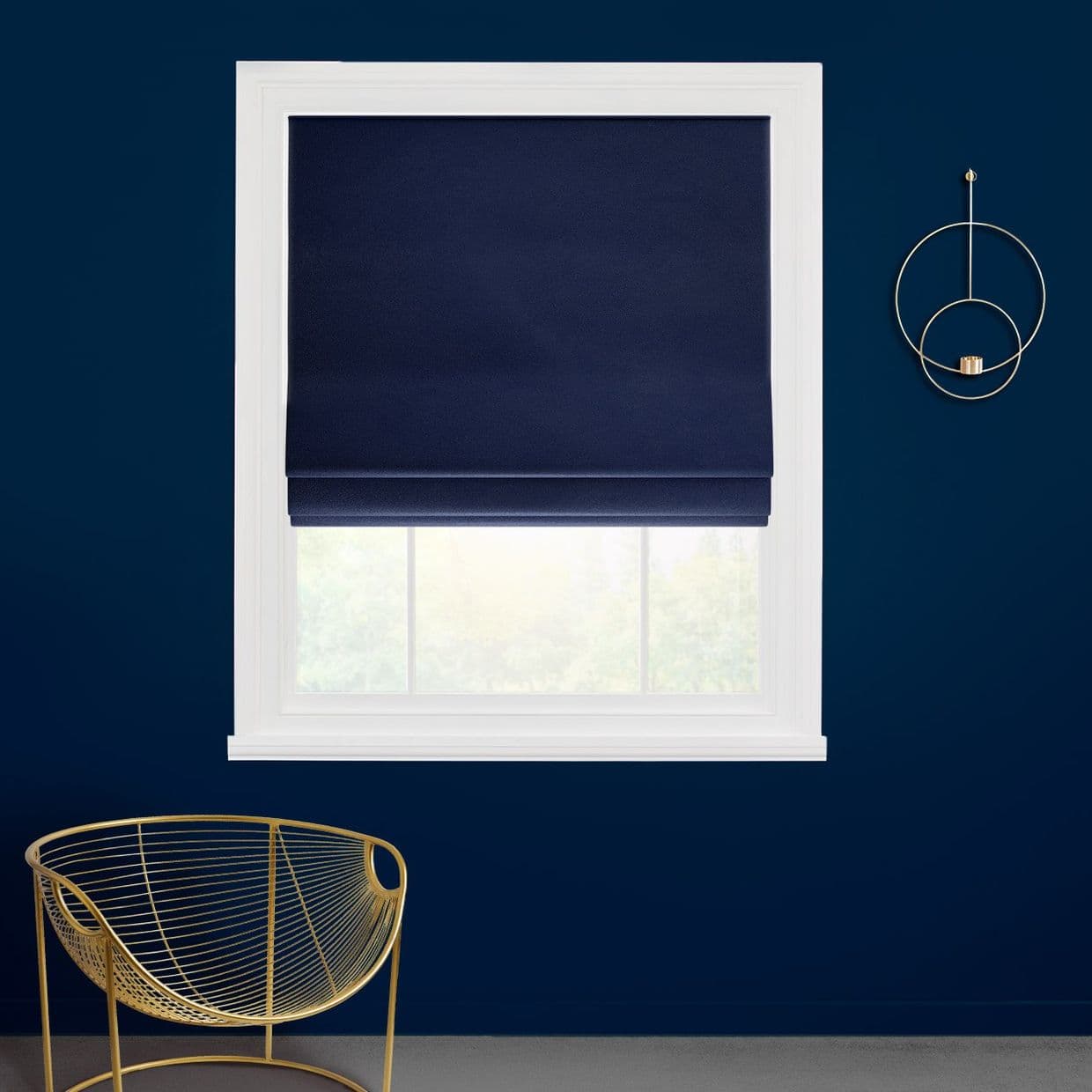 Navy Roman shade, lowered over the upper window, softly filtering daylight; in a white frame on a dark-blue wall beside a gold wire chair and wall ornament, faint garden view.