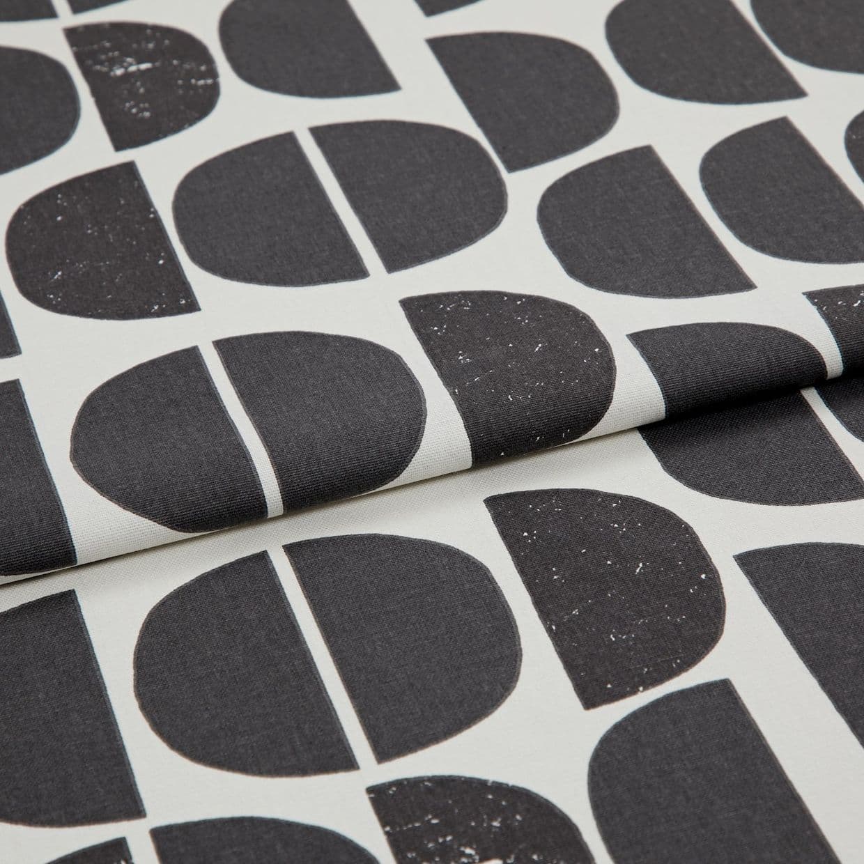 Folded printed fabric featuring large black semi-circles and vertical-split halves with subtle distressed speckling, folded over itself in a close-up studio shot with soft, even lighting.