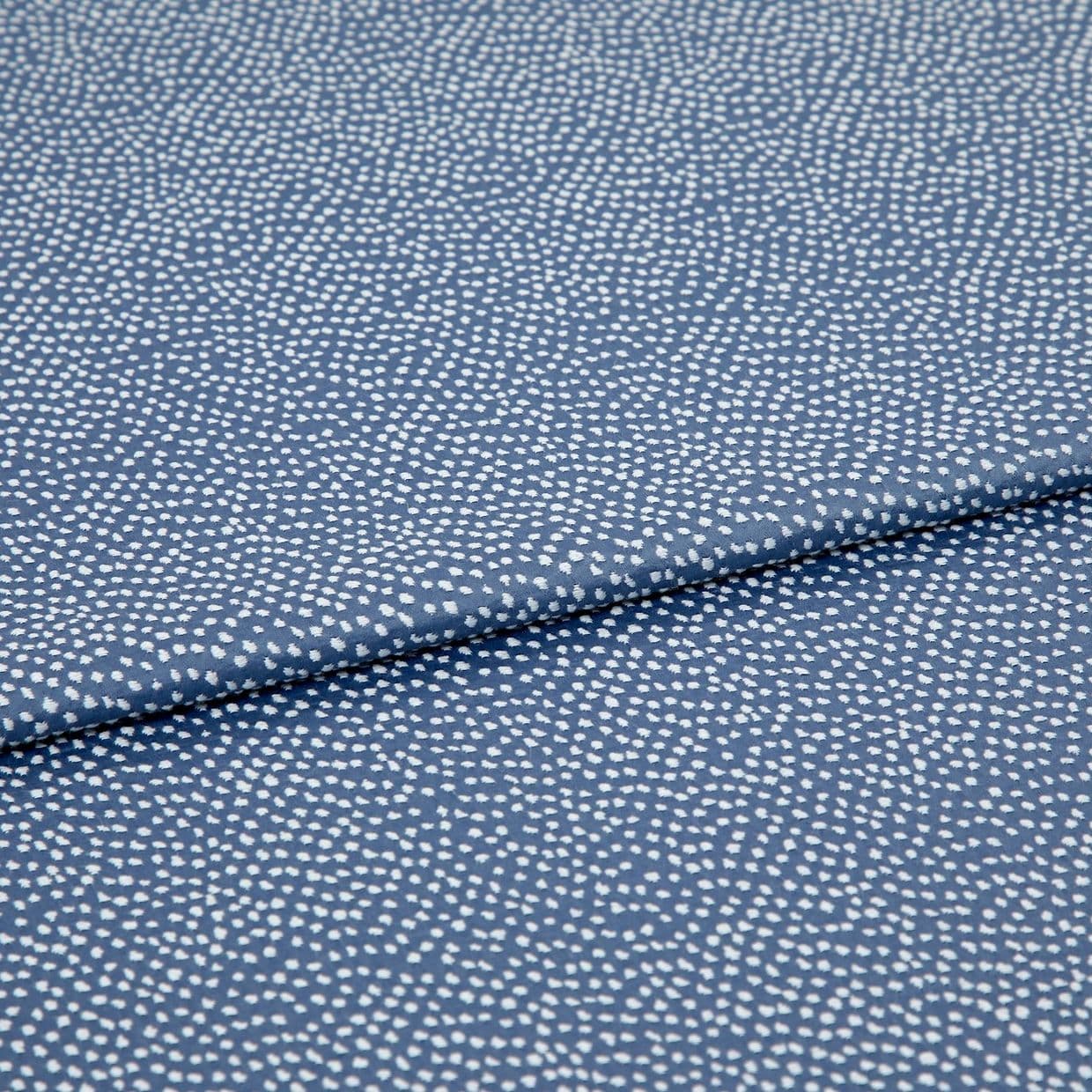 Blue fabric with dense, irregular white dot pattern, folded across the frame; lying flat and slightly overlapped, photographed close-up under soft, even studio lighting for a textile product shot.