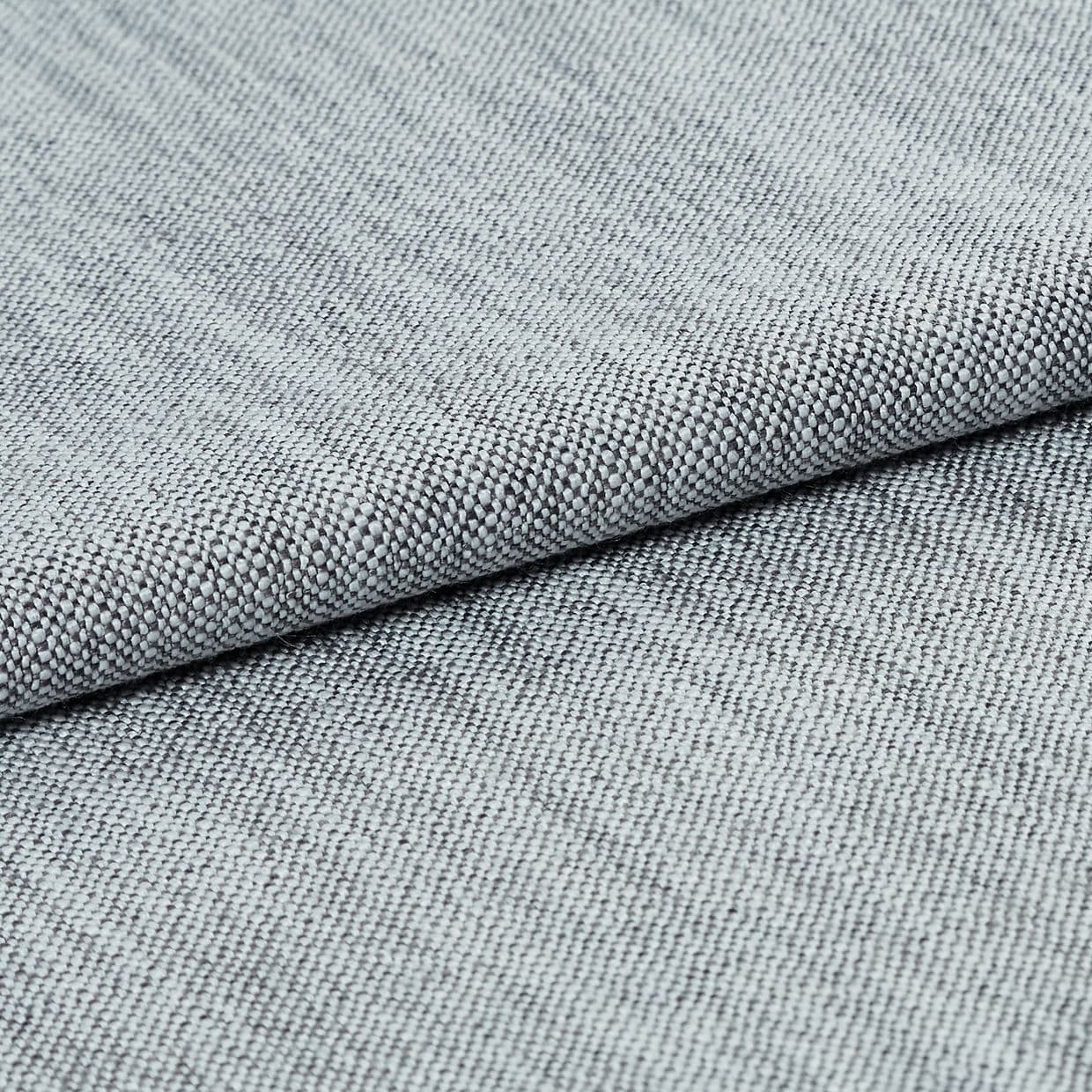 Light-gray tight basket-weave upholstery fabric, folded and layered to highlight its textured edge, photographed close-up under soft studio lighting on a neutral background.