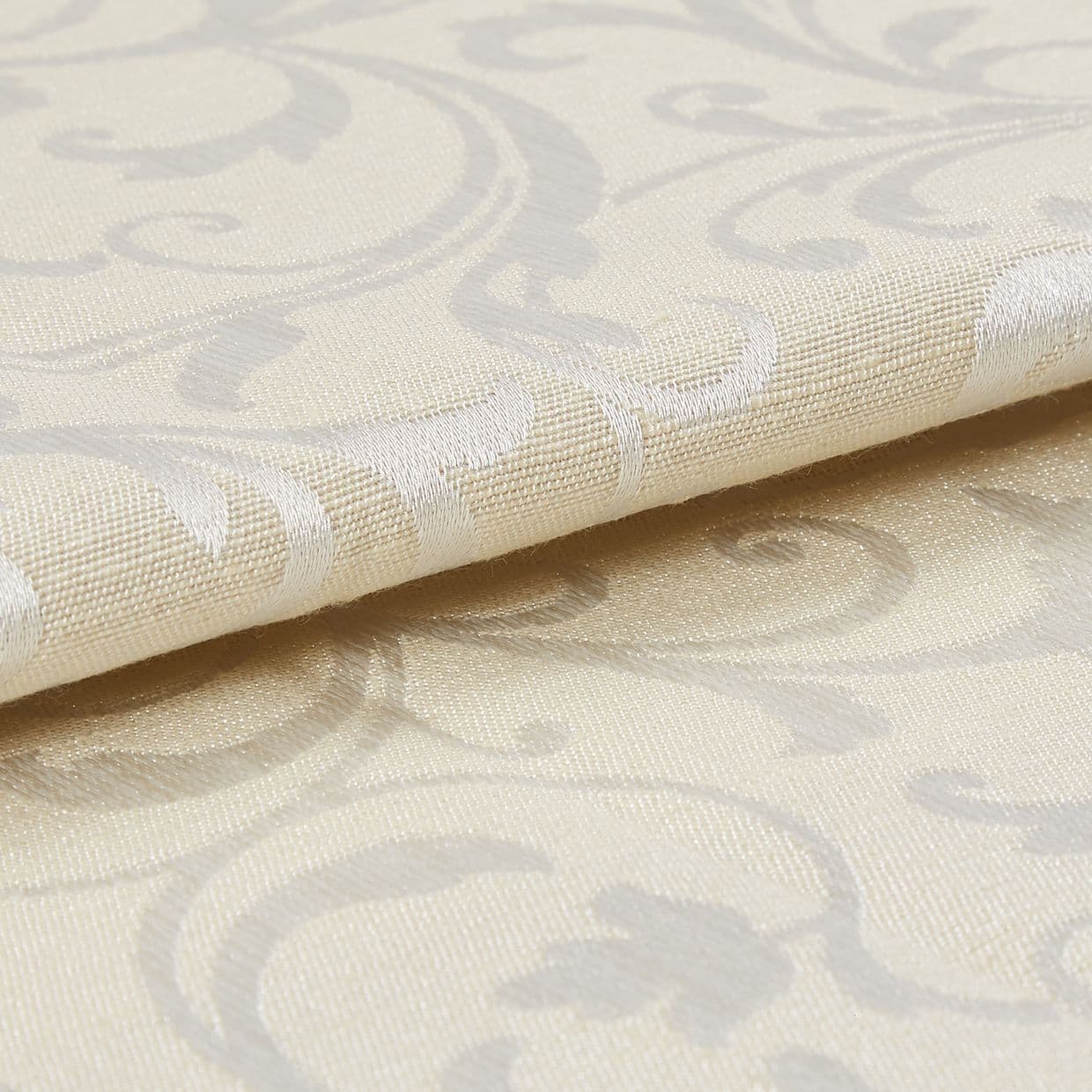 Cream damask curtain fabric swatch, folded with raised woven scroll motifs, reflecting subtle sheen; close-up macro view showing textured weave and soft studio lighting on a neutral surface.
