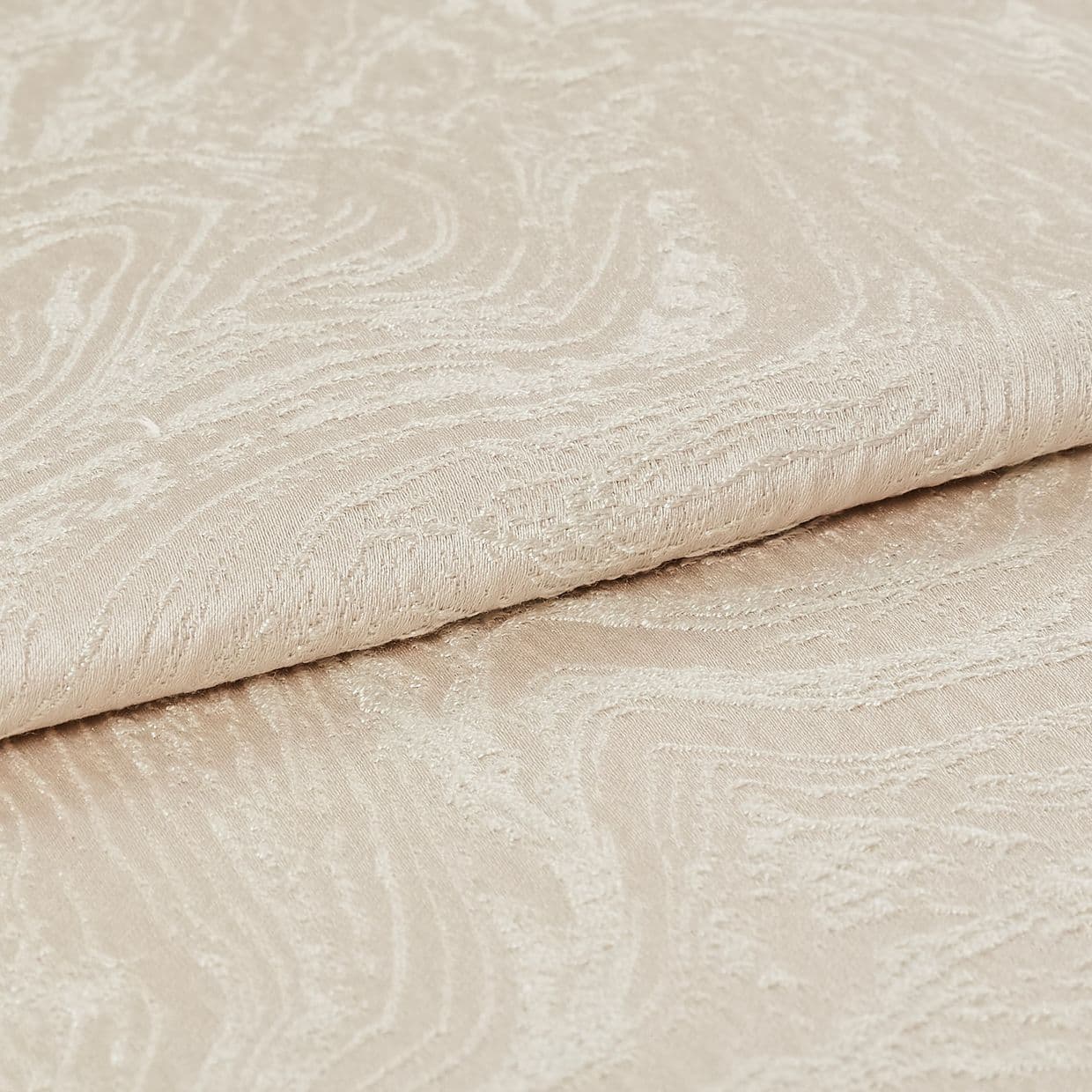 Beige jacquard fabric with subtle swirling embossed pattern, folded over itself; close-up view showing raised texture and soft sheen, neutral lighting on a plain surface.