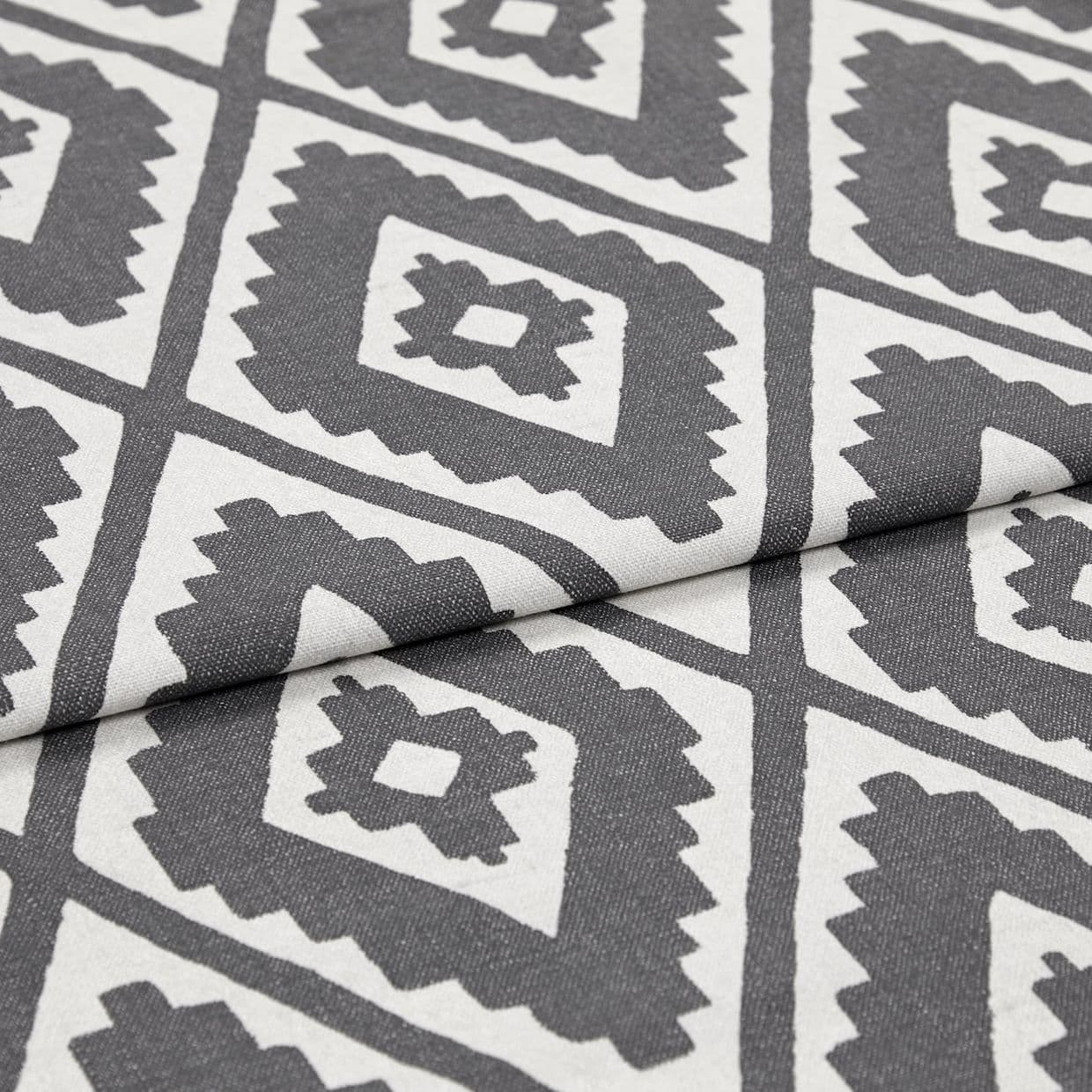 Gray-and-white printed upholstery fabric folded over itself, showing repeating serrated diamond motifs; close-up view highlights woven texture and subtle studio lighting on a neutral background.