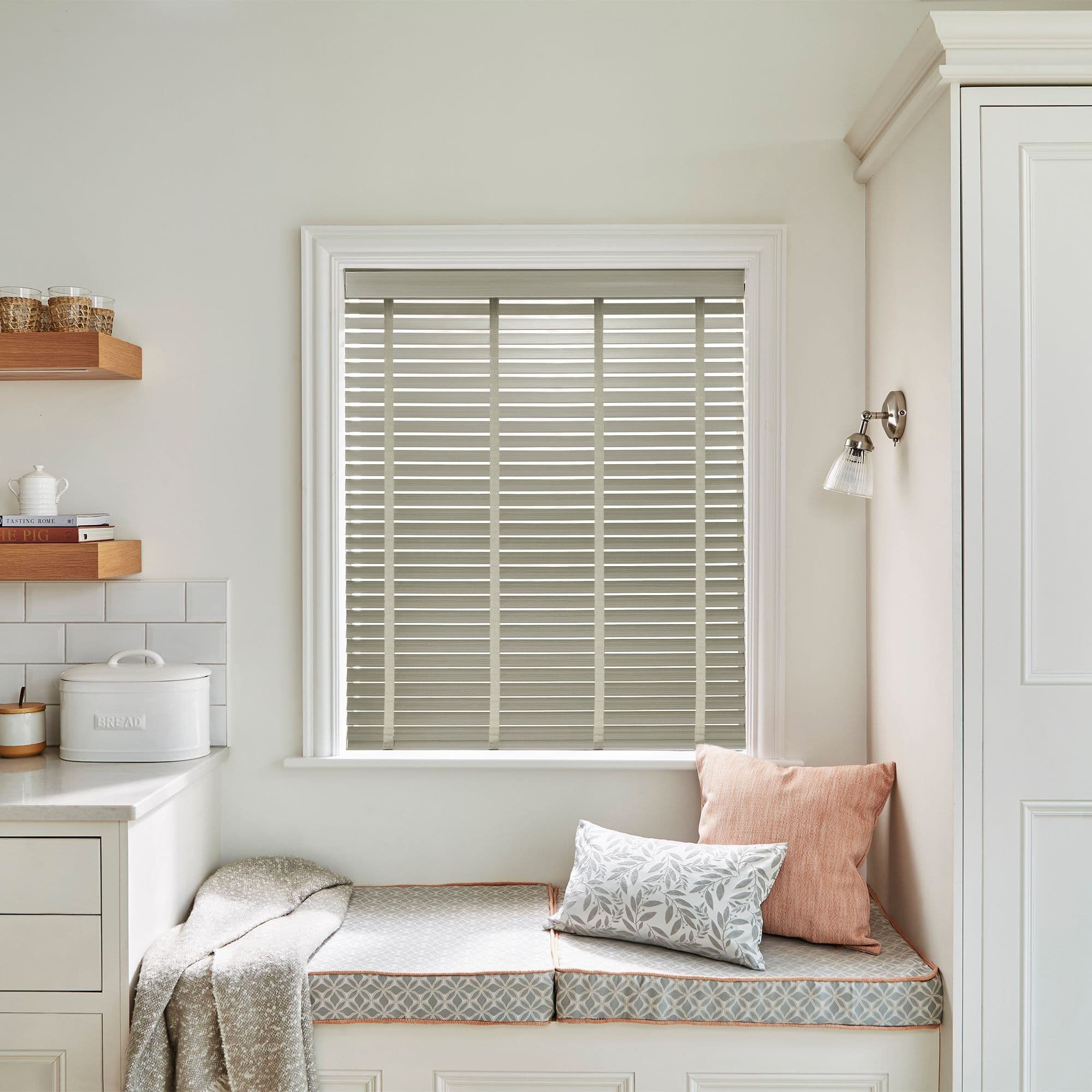 Horizontal slatted Venetian blinds (inside-mounted, beige-grey slats) closed, filtering soft daylight into a bright kitchen window seat with cushions, built-in bench, shelves, and pale walls.

Transcription: BREAD
TASTING ROME
THE PIG