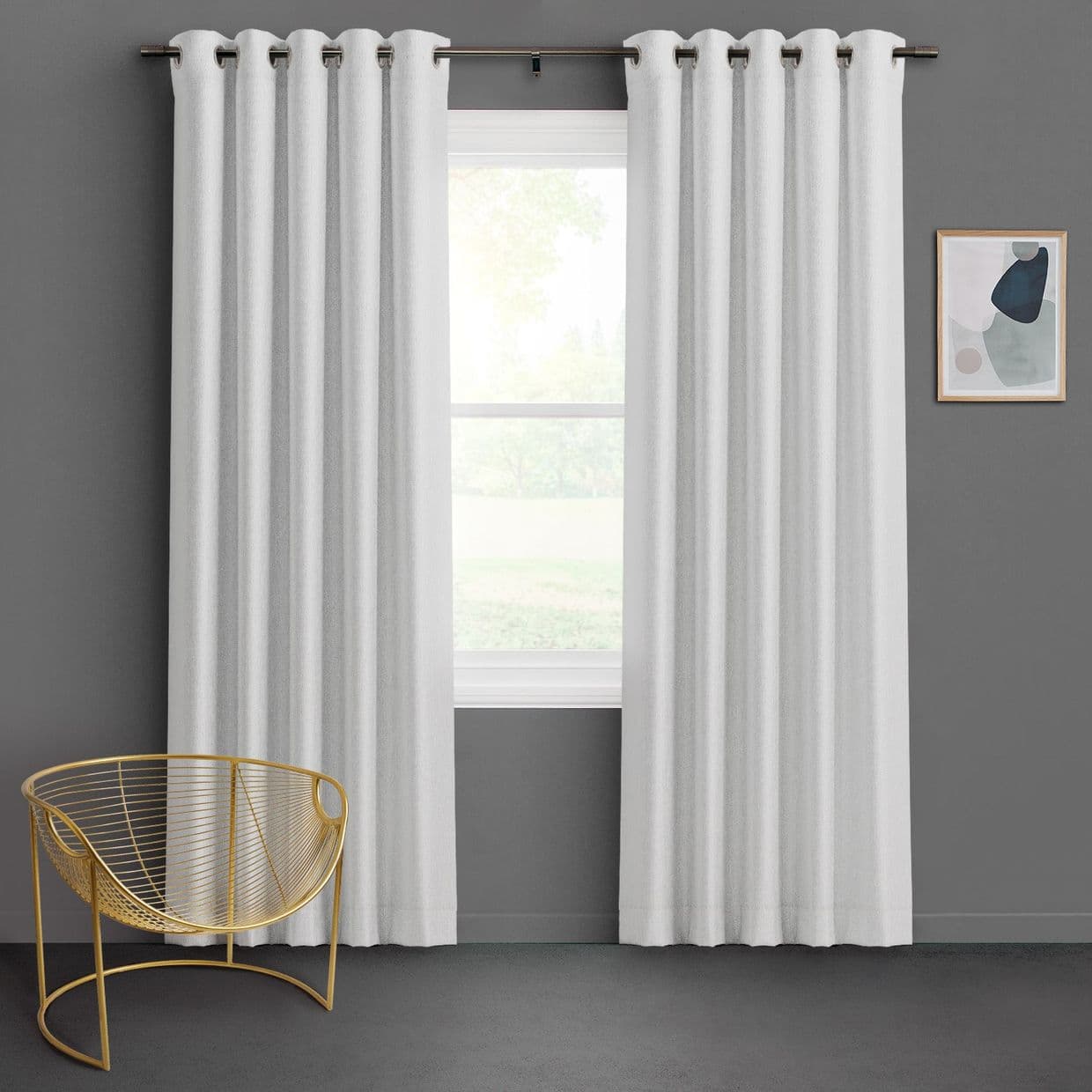 White grommet-top curtains, full-length, hung on a bronze rod and parted to reveal the window while filtering soft daylight; set against a dark gray wall in a minimal room with a gold wire chair and abstract art.