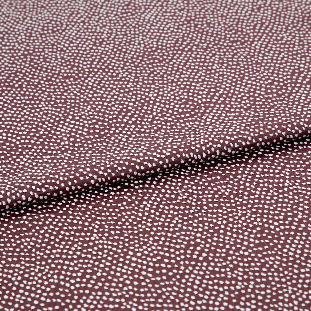 Burgundy fabric patterned with dense, irregular white dots, folded across the center; lying flat in a close-up studio shot, even lighting highlights its texture and subtle sheen.