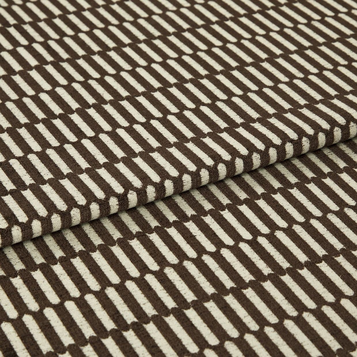 Brown-and-cream patterned textile (rectangular geometric motif) folded over itself; tufted loops create raised texture, shown in tight close-up under even studio lighting on a neutral background.
