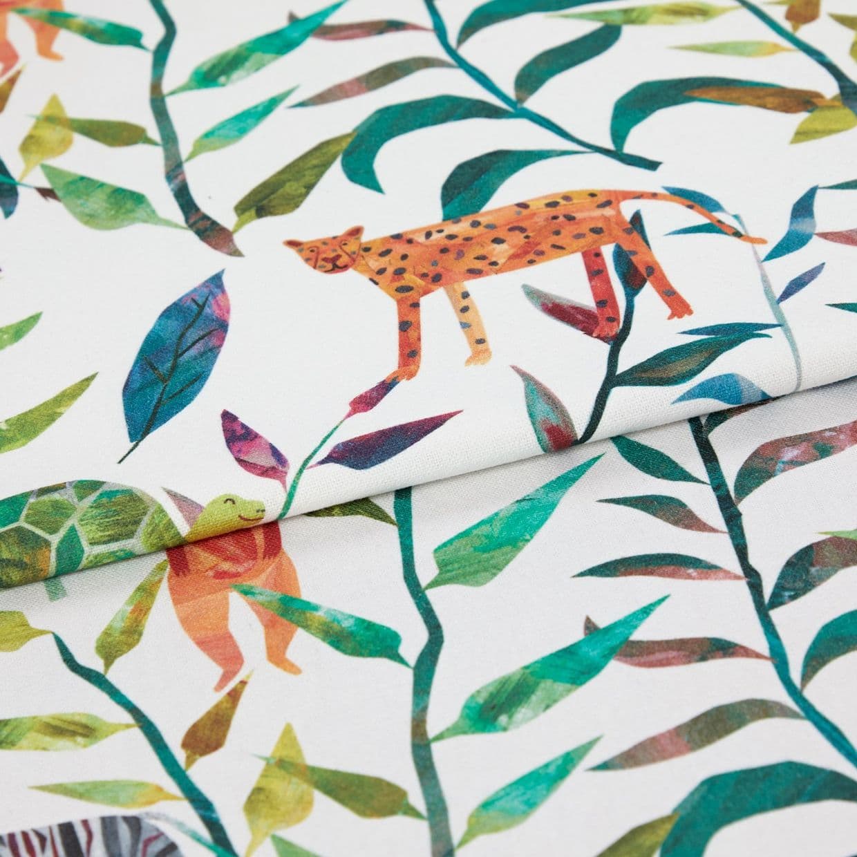 Printed cotton fabric with colorful leafy vines and stylized animals (cheetah, turtle), folded and layered, close-up on a white background under bright, even lighting.