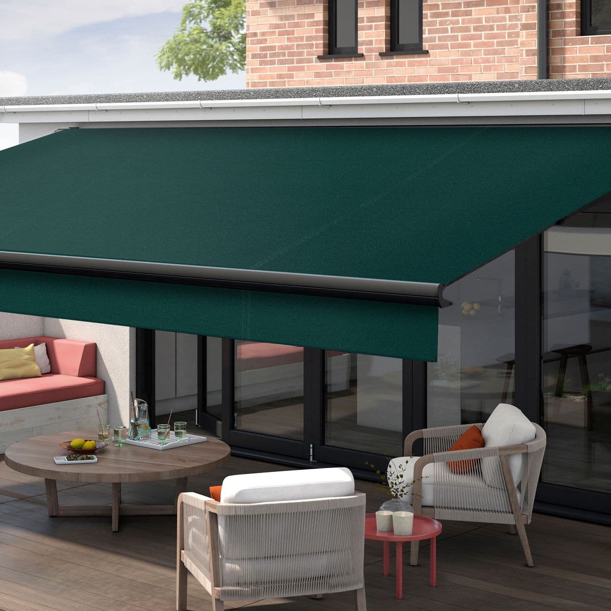 A deep-green fabric retractable awning, fully extended with metal bar, shading a patio and filtering daylight; wooden-deck terrace with cushioned chairs, round coffee table, bench by glass doors and brick wall.