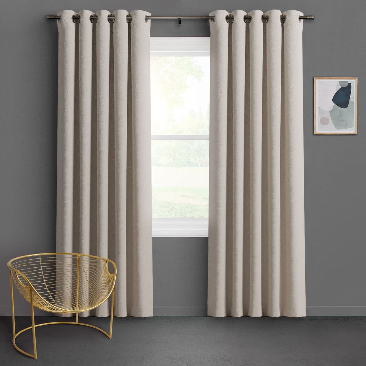 Cream grommet-top curtains, floor-length and pleated on a metal rod, parted to reveal bright window; hanging and filtering diffused daylight in a gray-walled minimalist room with gold wire chair.