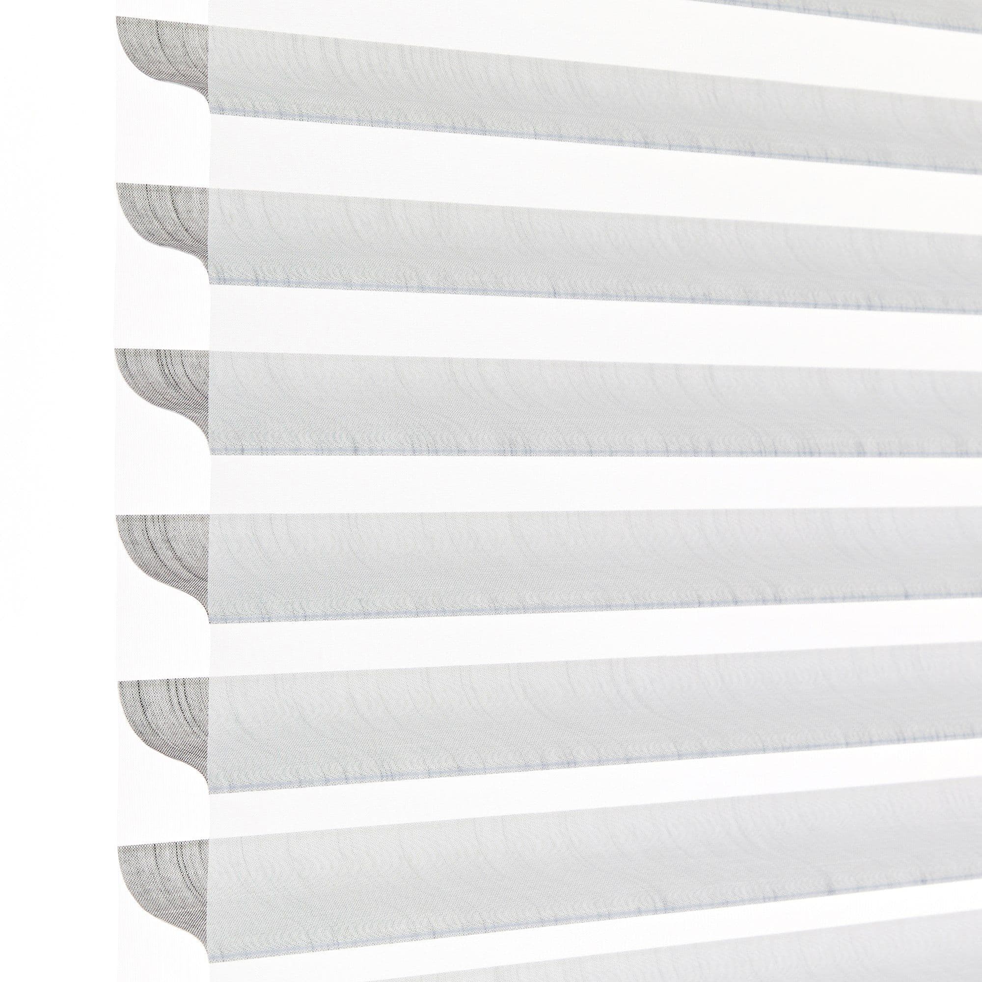 Horizontal zebra (dual-layer) roller blind at the left edge with alternating sheer and opaque stripes, aligned to filter and diffuse bright daylight; close-up, minimal interior against a white background.