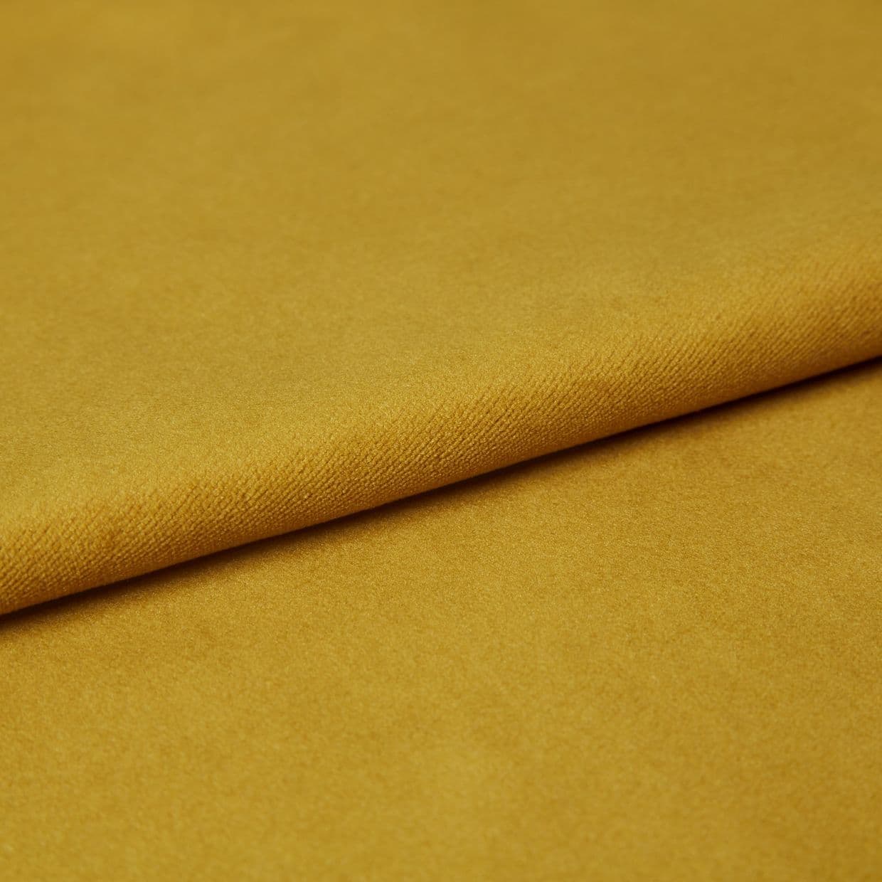 Mustard-yellow fabric, folded once with a visible textured edge, lying flat; soft pile catching even studio lighting, close-up composition emphasizing a smooth, plush surface.