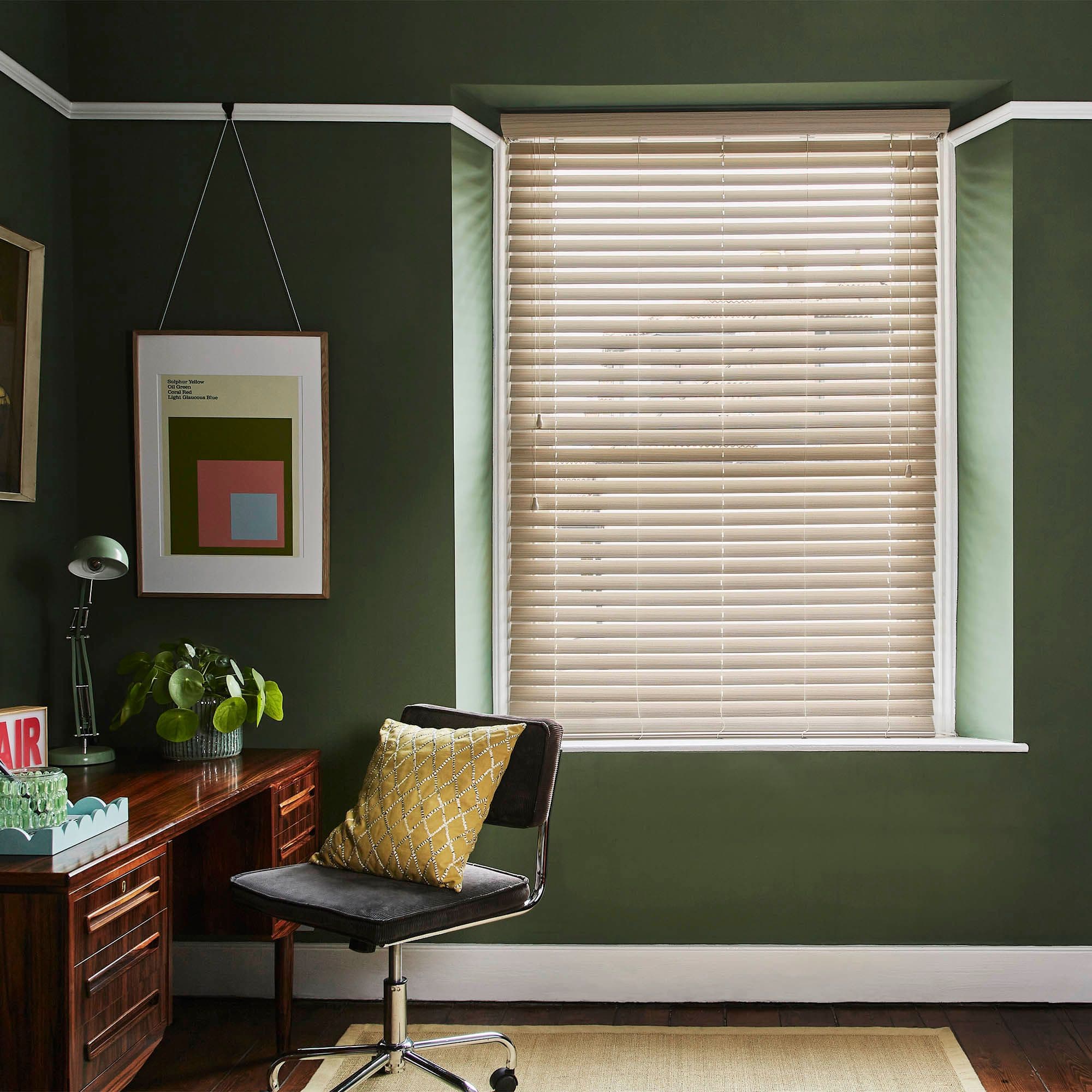 Beige horizontal venetian blinds mounted inside a window recess, slats mostly closed, filtering soft daylight; small dark-green home study with wooden desk, swivel chair and yellow cushion.

AIR